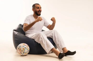 الحماس والتفاعل مع المنتخب ،إيماءات الشغف والتشجيع للفريق ، تنمية الهوايات الرياضية، مشاهدة ومتابعة مباراة كرة القدم ،  بورتريه لرجل عربي خليجي سعودي مبتسم يرتدي سروال وفانيلا باللون الأبيض يجلس على كرسي مريح يحمل الكرة ،  أنديه رياضية مختلفة، خلفية بيضاء .