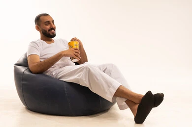 مفهوم التسليه والترفيه، قضاء أوقات ممتعة في عطلة نهاية الاسبوع، أنشطة وفعاليات مسلية،  بورتريه  لرجل عربي سعودي خليجي يرتدي سروال وفانيلا أبيض يجلس على كرسي مريح ويأكل الفوشار، تناول الوجبات الخفيفة والسناك، مفهوم الرجولة والثقة بالنفس، خلفية بيضاء