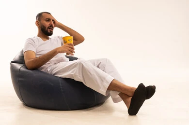 مشاعر اليأس والحزن يد على الرأس، مفهوم التسليه والترفيه، قضاء أوقات ممتعة في عطلة نهاية الاسبوع، أنشطة وفعاليات مسلية،  بورتريه  لرجل عربي سعودي خليجي يرتدي سروال وفانيلا أبيض يجلس على كرسي مريح ويأكل الفوشار، تناول الوجبات الخفيفة والسناك، خلفية بيضاء