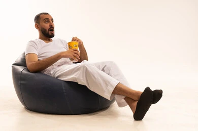 Expressions of astonishment and surprise, the concept of amusement and entertainment, spending enjoyable times on the weekend, fun activities and events, a portrait of an Arab Saudi Gulf man wearing white pants and a t-shirt sitting on a comfortable chair eating popcorn, snacking and light meals, white background.