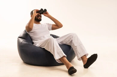 رؤية الاشياء البعيدة و تقريبها, التخطيط المستقبلي للأهداف والطموحات, مفهوم التسليه والترفيه، قضاء أوقات ممتعة في عطلة نهاية الاسبوع، أنشطة وفعاليات مسلية،  بورتريه لرجل عربي سعودي خليجي يرتدي سروال وفانيلا أبيض يجلس على كرسي مريح ويضع على عيونه منظار، خلفية بيضاء