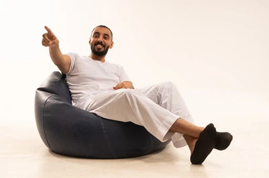 حركات وإيماءات تدل على الإشارة لشخص ما، الإشارة و التوضيح إلى شيء ما, تحديد موقع معين, الدلالة على مكان عنصر, الأناقة والاهتمام بالمظهر الخارجي, بورتريه من الخلف لرجل عربي سعودي خليجي يرتدي سروال وفانيلا أبيض يجلس على كرسي مريح ويشير بيده, ، خلفية بيضاء