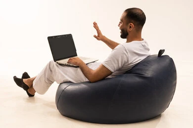 Professionalism in computer jobs and information technology, using modern technologies, utilizing modern technical devices, a portrait from behind of an Arab Saudi Gulf man wearing white pants and a white t-shirt sitting on a comfortable chair and working on a laptop, the concept of masculinity and self-confidence, white background.