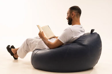 استغلال الوقت في التثقف، مفهوم التمعن والتركيز، مفهوم محو الأمية والتعلم، التخطيط المستقبلي للأهداف والطموحات, بورتريه من الخلف لرجل عربي سعودي خليجي يرتدي سروال وفانيلا أبيض يجلس على كرسي مريح ويمسك بيديه كتاب يقرأه بتمعن, ، خلفية بيضاء