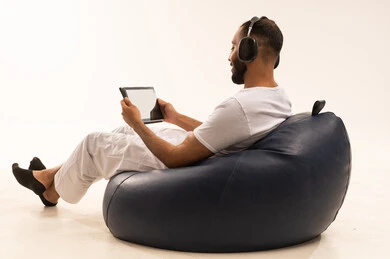 استعمال التقنيات الحديثة، استخدام الجهاز اللوحي(التابلت)، استخدام اجهزة تقنية حديثة، انهاء المهام اليومية من بعد، بورتريه من الخلف لرجل عربي سعودي خليجي يرتدي سروال وفانيلا أبيض يجلس على كرسي مريح ويضع سماعات الرأس ، مفهوم الرجولة والثقة بالنفس، خلفية بيضاء