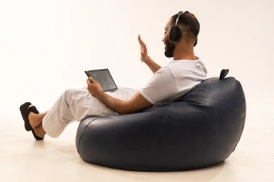 التحية والسلام عبر مكالمة فيديو باستخدام الجهاز اللوحي، استخدام اجهزة تقنية حديثة، انهاء المهام اليومية من بعد، بورتريه من الخلف لرجل عربي سعودي خليجي يرتدي سروال وفانيلا أبيض يجلس على كرسي مريح ويضع سماعات الرأس ، مفهوم الرجولة والثقة بالنفس، خلفية بيضاء