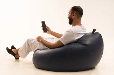 التواصل مع الأهل والأصدقاء باستخدام الجهاز المحمول، استخدام اجهزة تقنية حديثة، انهاء المهام اليومية من بعد، بورتريه من الخلف لرجل عربي سعودي خليجي يرتدي سروال وفانيلا أبيض يجلس على كرسي مريح ويحمل جهاز الهاتف المحمول ، مفهوم الرجولة والثقة بالنفس، خلفية بيضاء