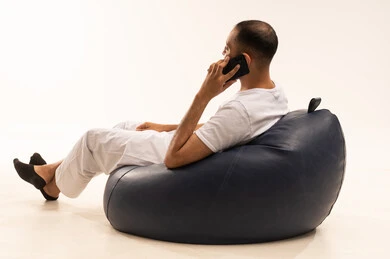 اجراء مكالمة هاتفية باستخدام الجهاز المحمول، استخدام اجهزة تقنية حديثة، انهاء المهام اليومية من بعد، بورتريه من الخلف لرجل عربي سعودي خليجي يرتدي سروال وفانيلا أبيض يجلس على كرسي مريح ويحمل جهاز الهاتف المحمول ، مفهوم الرجولة والثقة بالنفس، خلفية بيضاء