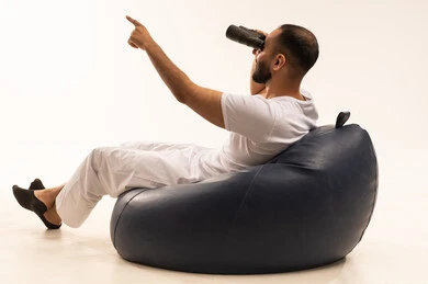 توضيح الرؤية وتقريبها عبر التلسكوب, حب الاستكشاف والمغامرة، رؤية الاشياء البعيدة و تقريبها, التخطيط المستقبلي للأهداف والطموحات, بورتريه من الخلف لرجل عربي سعودي خليجي يرتدي سروال وفانيلا أبيض يجلس على كرسي مريح ويضع على عيونه منظار، خلفية بيضاء