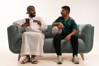 Using the phone to store information and data, interacting by watching the favorite team, gestures of challenge and victory, spending enjoyable leisure time with friends, recreational sports activities, a portrait of two Arab Gulf Saudi men, one of whom is a young Saudi wearing the Saudi national team jersey, white background. Using the phone to store information and data, interacting by watching the favorite team, gestures of challenge and victory, spending enjoyable leisure time with friends, recreational sports activities, a portrait of two Arab Gulf Saudi men, one of whom is a young Saudi wearing the Saudi national team jersey, white background.
