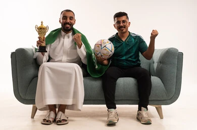 رفع قبضة اليد بتعابير الفوز والانتصار، الشغف في متابعة فريق المنتخب الوطني، أنشطة رياضية ترفيهية، بورتريه لرجلين عربيين خليجيين سعوديين احدهما يضع على أكتافه علم المملكة ويحمل كأس ذهبي، شاب سعودي يرتدي قميص المنتخب السعوديي ويحمل كرة،خلفية بيضاء