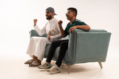 رفع قبضة اليد بتعابير الفوز والانتصار، الشغف في متابعة فريق المنتخب الوطني، أنشطة رياضية ترفيهية، مفهوم الفوز و الانتصار في المباريات،  بورتريه من الجانب لرجلين عربيين خليجيين سعوديين احدهما يحمل كرة، شاب سعودي يرتدي قميص المنتخب السعوديي، خلفية بيضاء