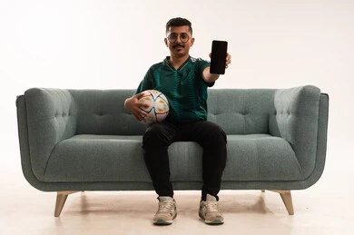 دمج التقنيات الحديثة مع الحياة اليومية، عرض شاشة سوداء على الهاتف، التفاعل بمشاهدة الفريق المفضل, ايماءات التحدي والانتصار، قضاء اوقات الفراغ الممتعة مع الاصدقاء، أنشطة رياضية ترفيهية،  بورتريه لشاب سعودي يرتدي قميص المنتخب السعوديي ويحمل بيده كرة، خلفية بيضاء