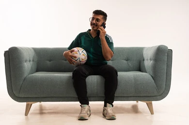 اجراء مالمة هاتفية، دمج التقنيات الحديثة مع الحياة اليومية، التفاعل بمشاهدة الفريق المفضل, ايماءات التحدي والانتصار، قضاء اوقات الفراغ الممتعة مع الاصدقاء، أنشطة رياضية ترفيهية،  بورتريه لشاب سعودي يرتدي قميص المنتخب السعوديي ويحمل بيده كرة، خلفية بيضاء