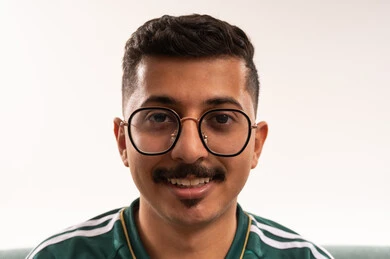 النظر إلى الكاميرا بايماءات السرور الثقة، التفاعل بمشاهدة الفريق المفضل, ايماءات التحدي والانتصار، الألعاب والمباريات الرياضية, أنشطة رياضية ترفيهية،  بورتريه مقرب لشاب سعودي يرتدي قميص المنتخب السعوديي ويضع نظارة طبية، خلفية بيضاء