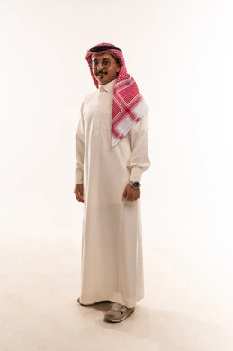 الوقوف باستقامة والنظر إلى الكاميرا بتعابير السرور، بورتريه لشاب عربي خليجي سعودي يرتدي الثوب والشماغ التقليدي ويضع النظارة الطبية، الاناقة والاهتمام بالمظهر الخارجي، الطول الكامل للجسم، خلفية بيضاء