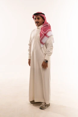 الوقوف باستقامة والنظر إلى شيء ما، بورتريه لشاب عربي خليجي سعودي يرتدي الثوب والشماغ التقليدي، الاناقة والاهتمام بالمظهر الخارجي، الطول الكامل للجسم، خلفية بيضاء