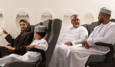 Spending the summer vacation with family, a family tourist trip, an Arab Gulf Omani woman wearing a hijab and abaya with her son on the plane, pointing to something, two Arab Gulf men wearing dishdasha and kumma discussing and exchanging opinions, Oman Air.
