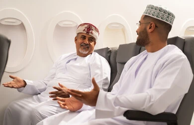 القيام بالحوارات والنقاشات, الاستمتاع بقضاء وقت ممتع اثناء رحله السفر , ايماءات السعادة و السرور , رجلان عربيان خليجيان عمانيان يرتديان الدشداشة و الكمه يجلسان داخل الطائرة فر رحله جوية , مفهوم السياحه و السفر