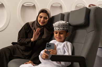 الأجواء العائلية السعيدة, توثيق اللحظات المميزة باستخدام الأجهزة التقنية الحديثة, قضاء الأوقات الممتعة مع الأبناء, امرأة عربية خليجية إماراتية مع ابنها داخل الطائرة فى رحله جوية يرتديان الزي التقليدي الماني يقومان بالتقاط صور السيلفي التذكارية عبر الجوال, مفهوم السياحة و السفر