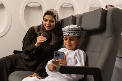 Documenting special moments using modern technological devices, spending enjoyable times with children, an Arab Gulf Emirati woman with her son inside an airplane on a flight, both wearing traditional German attire, taking commemorative selfies with a mobile phone, happy family atmosphere, the concept of tourism and travel.