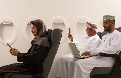 استخدام جهاز تقني حديث ومتطور في الحياة اليومية, تصفح وسائل التواصل الاجتماعي, الدردشة مع العائلة والأصدقاء, امراة عربية خليجيه عمانية ترتدي الحجاب و العباءة تجلس داخل الطائرة فى رحلة جوية , رجل خليجي مسن يرتدي الدشداشة و الكمه يقوم بالتقاط صورة سيلفي عبر الهاتف المحمول , مفهوم السياحة و السفر
