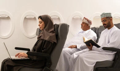 إنجاز مهام العمل عن بعد من خلال الانترنت، إجراء مكالمات فيديو عبر جهاز اللابتوب، شابة عربية خليجية عمانية ترتدي العباءة و الحجاب تجلس داخل الطائرة فى رحلة جوية تعمل على الحاسب المحمول, رجل خليجي يرتدي الدشادشة و الكمه يقوم بقراءة كتاب، استخدام التكنولوجيا الحديثة والمتطورة, مفهوم السياحة و السفر