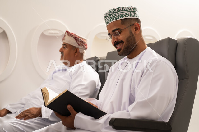 ثقافة التعلم الذاتي, قضاء وقت الفراغ بالتعلم والثقافة, ممارسة هواية المطالعة, رجل عربي خليجي عماني يرتدي الدشداشة و الكمه يجلس داخل الطائرة فى رحله جويه برفقه والده المسن , مفهوم السياحة و السفر