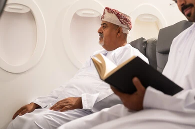 قضاء وقت الفراغ بالتعلم والثقافة, ممارسة هواية المطالعة، ثقافة التعلم الذاتي, رجل عربي خليجي عماني يرتدي الدشداشة و الكمه يجلس داخل الطائرة فى رحله جويه برفقه والده المسن , مفهوم السياحة و السفر