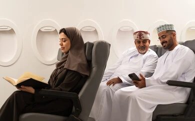 الاستمتاع بالقراءة وتوسيع المعرفة,مشاهده الافلام و المسرحيات عبر الجوال , رجلان عربيان خليجيان عمانيان يرتديان الدشداشة و الكمه يجلسان داخل الطائرة فى رحله جوية , امراة خليجية تقوم بقراءة كتاب,  ايماءات السعادة و السرور , مفهوم السياحه و السفر