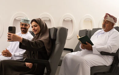 حفظ وتوثيق اللحظات السعيدة مع الزوج, عائلة عربية خليجيه عمانية ترتدي الزي التقليدي تجلس داخل الطائرة فى رحله جوية , امراة عربيه خليجيه امارتية تقوم بالتقاط صورة سيلفي عبر الهاتف المحمول برفقة زوجها , مفهوم السياحة و السفر , ايماءات السعادة و السرور