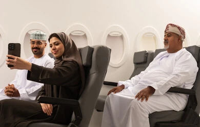 تصوير اللحظات العائلية المميزة, عائلة عربية خليجيه عمانية ترتدي الزي التقليدي تجلس داخل الطائرة فى رحله جوية , امراة عربيه خليجيه امارتية تقوم بالتقاط صورة سيلفي عبر الهاتف المحمول برفقة زوجها , مفهوم السياحة و السفر , ايماءات السعادة و السرور