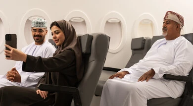 قضاء وقت ممتع اثناء السفر , عائلة عربية خليجيه عمانية ترتدي الزي التقليدي تجلس داخل الطائرة فى رحله جوية , امراة عربيه خليجيه امارتية تقوم بالتقاط صورة سيلفي عبر الهاتف المحمول برفقة زوجها , مفهوم السياحة و السفر , ايماءات السعادة و السرور