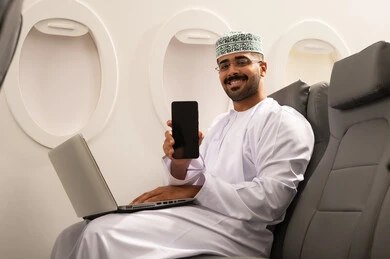عرض شاشة فارغة سوداء عبر الجوال , التواصل مع الأهل والاصدقاء عبر اللابتوب، انجاز مهام العمل عن بعد بايماءات الاندماج، رجل عربي خليجي عماني يرتدي االدشداشة و الكمة يجلس في الطائرة ويعمل على الحاسب المحمول، استخدام الأجهزة والتقنيات الحديثة، مفهوم السياحة والسفر