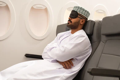 وسائل مواصلات جوية, ايماءات تدل على النوم والاسترخاء ، رجل عربي خليجي عماني يرتدي الدشداشة و الكمة يضع قناع النوم على عينيه يجلس في مقصورة الطائرة ، الشعور بالتعب والارهاق  ، خطوط الطيران الجوي ، سياحة وسفر ، رحلات جوية سياحية