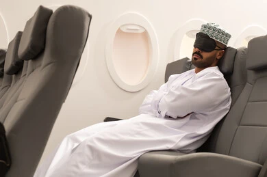 Gestures indicating sleep and relaxation, an Arab Gulf Omani man wearing a dishdasha and a kumma puts a sleep mask over his eyes sitting in the airplane cabin, feeling tired and exhausted, air transportation means, airline companies, tourism and travel, tourist flights.