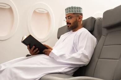ممارسة هواية القراءه, خطوط الطيران العماني, قضاء أوقات ممتعه في مقصورة الطائرة, قراءة الكتب المفيدة للتعلم والتثقف, رجل عربي خليجي عماني يرتدي الدشداشة و الكمه يجلس فى مقعد الطائرة,  الاستعداد لقضاء عطله صيفية
