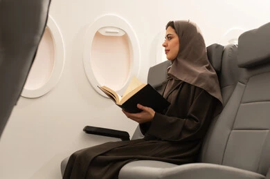 ممارسة هواية القراءه, قضاء أوقات ممتعه في مقصورة الطائرة, قراءة الكتب المفيدة للتعلم والتثقف, امراة عربيه هليجيه عمانية ترتدي الحجاب و العباءة تجلس فى مقعد الطائرة, قضاء عطله صيفية, خطوط الطيران العماني