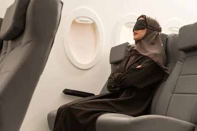 الشعور بالارهاق والتعب اثناء السفر, رحلات جوية سياحية, امراة عربية خليجية عمانية محجبة  ترتدي العباءة تضع قناع النوم على عينيها  تجلس داخل مقصورة الطائرة ، ايماءات تدل على النوم والاسترخاء ، وسائل مواصلات جوية ، خطوط الطيران الجوي ، سياحة وسفر