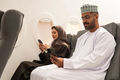 تصفح تطبيقات الهاتف المحمول، الدردشة والتحدث مع الاصدقاء عبر الانترنت، زوجان عربيان خليجيان عمانيان يرتديان الزي التقليدي يجلسان داخل الطائرة فى رحله جوية يقومان بمتابعة اخبار وسائل التواصل الاجتماعي باستخدام الجوال، ايماءات الاندماج والتركيز, مفهوم السياحة و السفر
