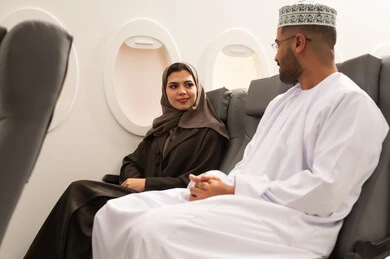 Joint discussions and dialogues, having a good time during travel, an Omani Gulf Arab couple wearing traditional attire sitting inside the airplane on a flight, the concept of tourism and travel. Joint discussions and dialogues, having a good time during travel, an Omani Gulf Arab couple wearing traditional attire sitting inside the airplane on a flight, the concept of tourism and travel.