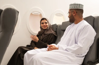 الدردشات والحوارات المتبادلة, قضاء وقت ممتع خلال فترة السفر, زوجان عربيان خليجيان عمانيان يرتديان الزي التقليدي يجلسان داخل الطائرة فى رحله جوية, مفهوم السياحه و السفر