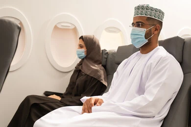 Having a good time during travel, an Arab Gulf couple from Oman wearing traditional attire and protective masks sitting inside the airplane on a flight, taking precautions against the spread of the coronavirus, the concept of tourism and travel.