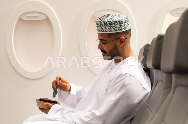 الاستمتاع باكل حلويات باردة,  صورة من الجانب لرجل عربي خليجي عماني يرتدي الدشداشة و الكمة يقضي أوقات ممتعة داخل الطائرة، تشيز كيك مع طبقات الكريمه، حلويات وسكريات، ايماءات وجه سعيدة