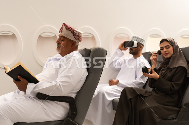 Enjoyment and entertainment in free time, the concept of tourism and travel, a Gulf Arab Omani family wearing traditional attire sitting inside an airplane on a flight, a Gulf woman applying makeup, the concept of tourism and travel.
