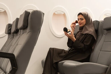 الاهتمام بالهيئة والأناقة, استخدام المساحيق التجميلية, مفهوم التزين والتجمل, امرأة عربية خليجية عمانية محجبة ترتدي العباءة  تجلس داخل الطائرة فى رحله جوية تستعمل فرشاة أحمر الخدود, شابة سعودية تضع المكياج, مفهوم السياحة و السفر