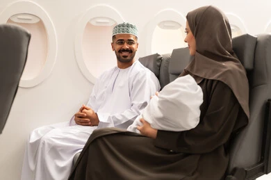 Taking tourist trips during vacation, the concept of motherhood and childcare, an Omani Gulf Arab family wearing traditional attire sitting inside an airplane on a flight, a Gulf mother holding her infant, the tenderness of mothers and their care for their children.