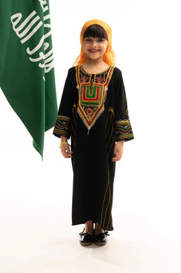 The anniversary of the founding of the first Saudi state on February 22, wearing the costumes of the southern region on national occasions, a portrait of a Saudi Gulf Arab girl wearing a sheila and a sidrah, looking at the camera with happy gestures and standing next to the founding flag, the day of our beginnings 1727 AD, full-length body, white background