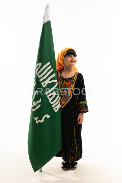 يوم بدينا 1727م, ذكرى تأسيس الدولة السعودية الأولى في 22 فبراير, ارتداء أزياء المنطقة الجنوبية في اليوم الوطني, بورتريه لفتاة عربية خليجية سعودية ترتدي الشيلة والسدرة تقف بجانب علم التأسيس بإيماءات السعادة والفخر, الجسم بالطول الكامل, خلفية بيضاء