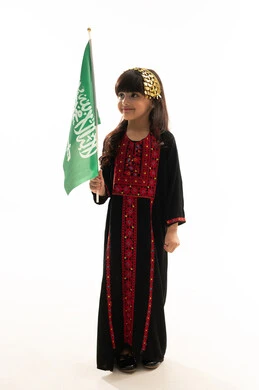 يوم العلم 11مارس، اليوم الوطني السعودي 23سبتمبر، ارتداء زي المنطقة الشمالية, يوم بدينا 1727م, ذكرى تأسيس الدولة السعودية الأولى في 22 فبراير, بورتريه لفتاة عربية خليجية سعودية مبتسمة ترتدي المحوثل تحمل العلم السعودي بفخر وشموخ, الجسم بالطول الكامل, خلفية بيضاء